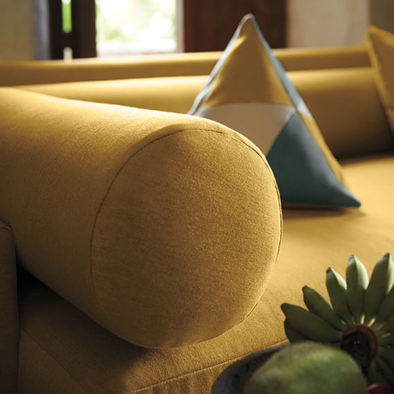 Close up of corner of yellow sofa and yellow bolster pillow.
