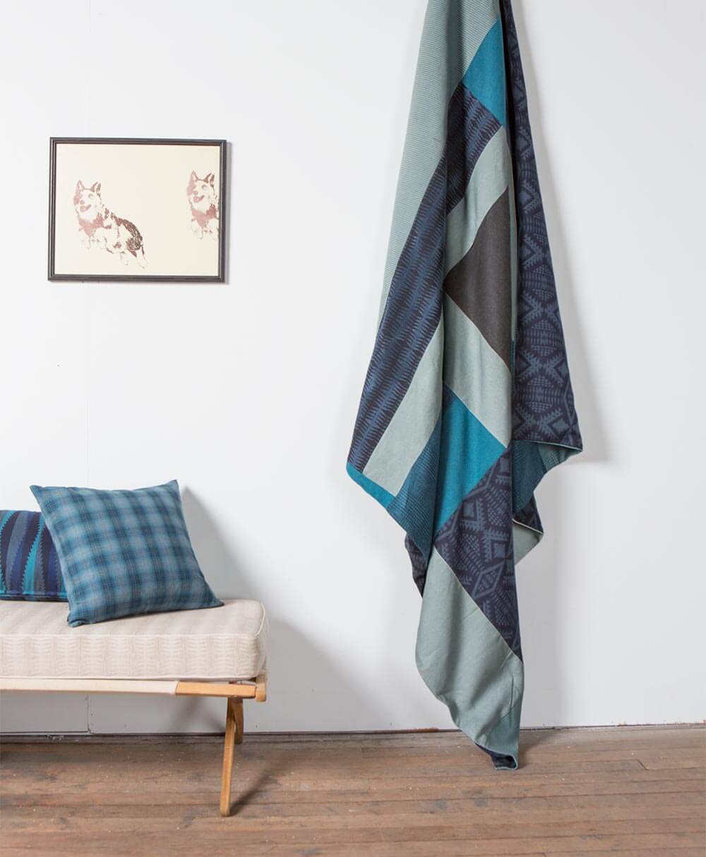 Édredon fabriqué avec des morceaux de tissus d’ameublement Pendleton par Sunbrella accroché au plafond à côté d’oreillers à motifs bleus.