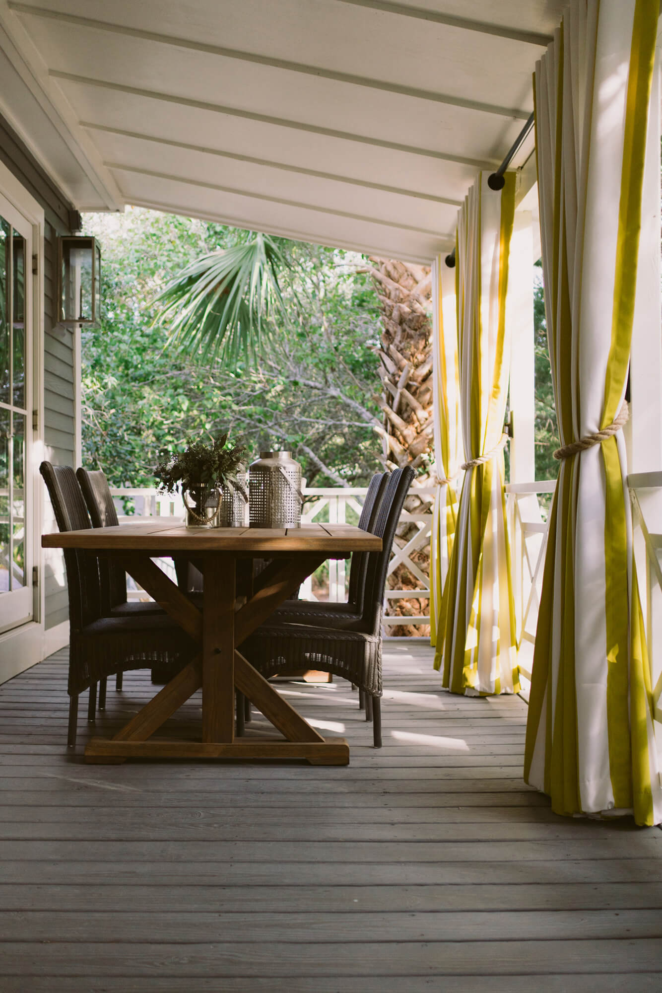 Uma mesa de jantar na varanda protegido por cortinas listradas amarelas e brancas feitas com tecido de estofado Sunbrella