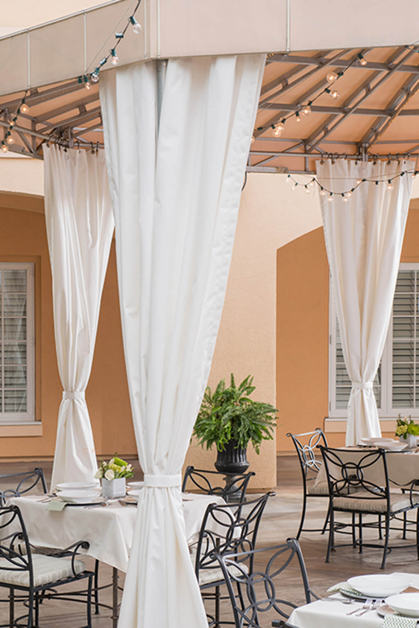 Il patio di un ristorante riceve ombra da una tenda a struttura fissa realizzata usando tessuti Sunbrella Clarity beige.