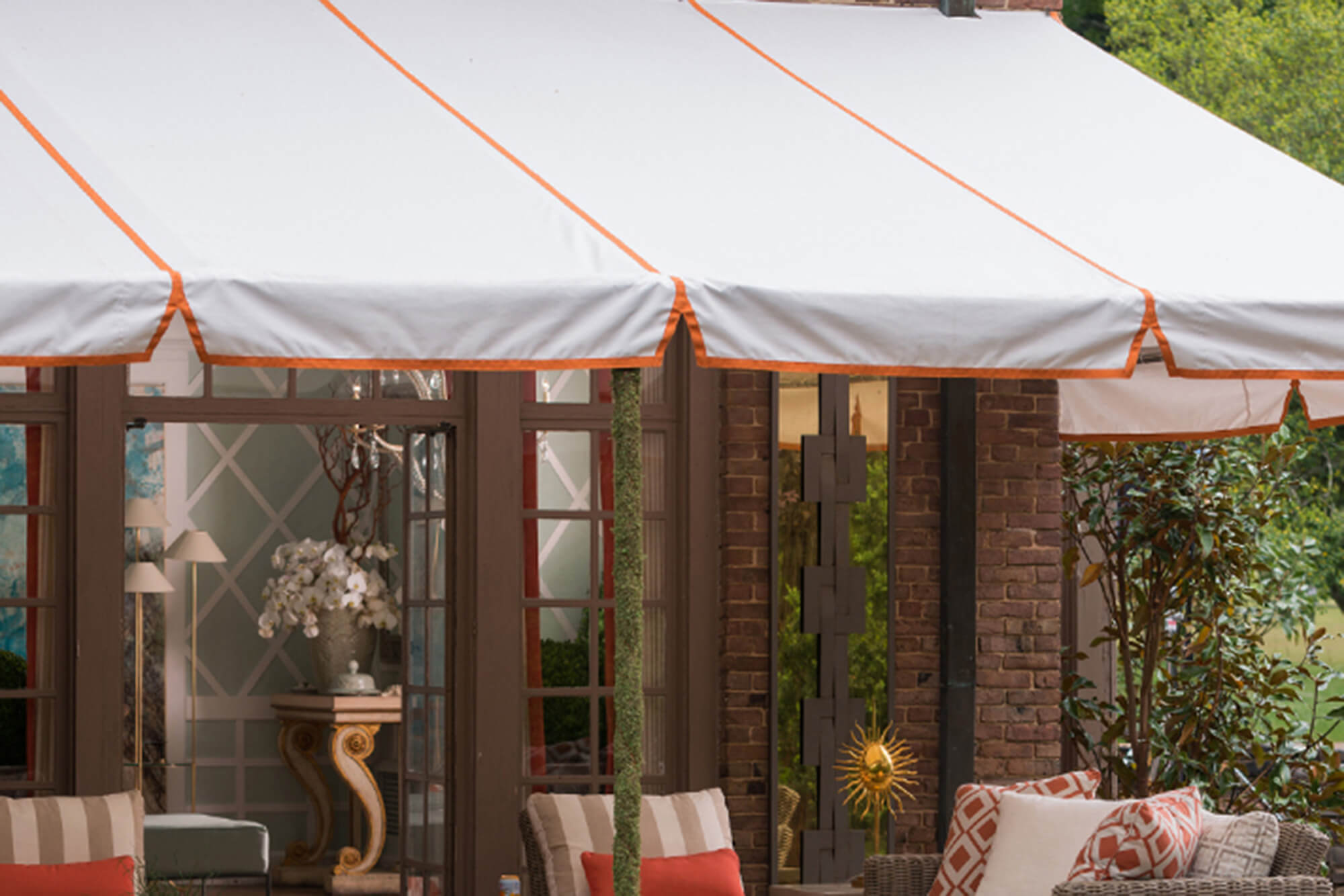 Un patio cubierto por un toldo de marco fijo con tela Sunbrella blanca y vivos en naranja