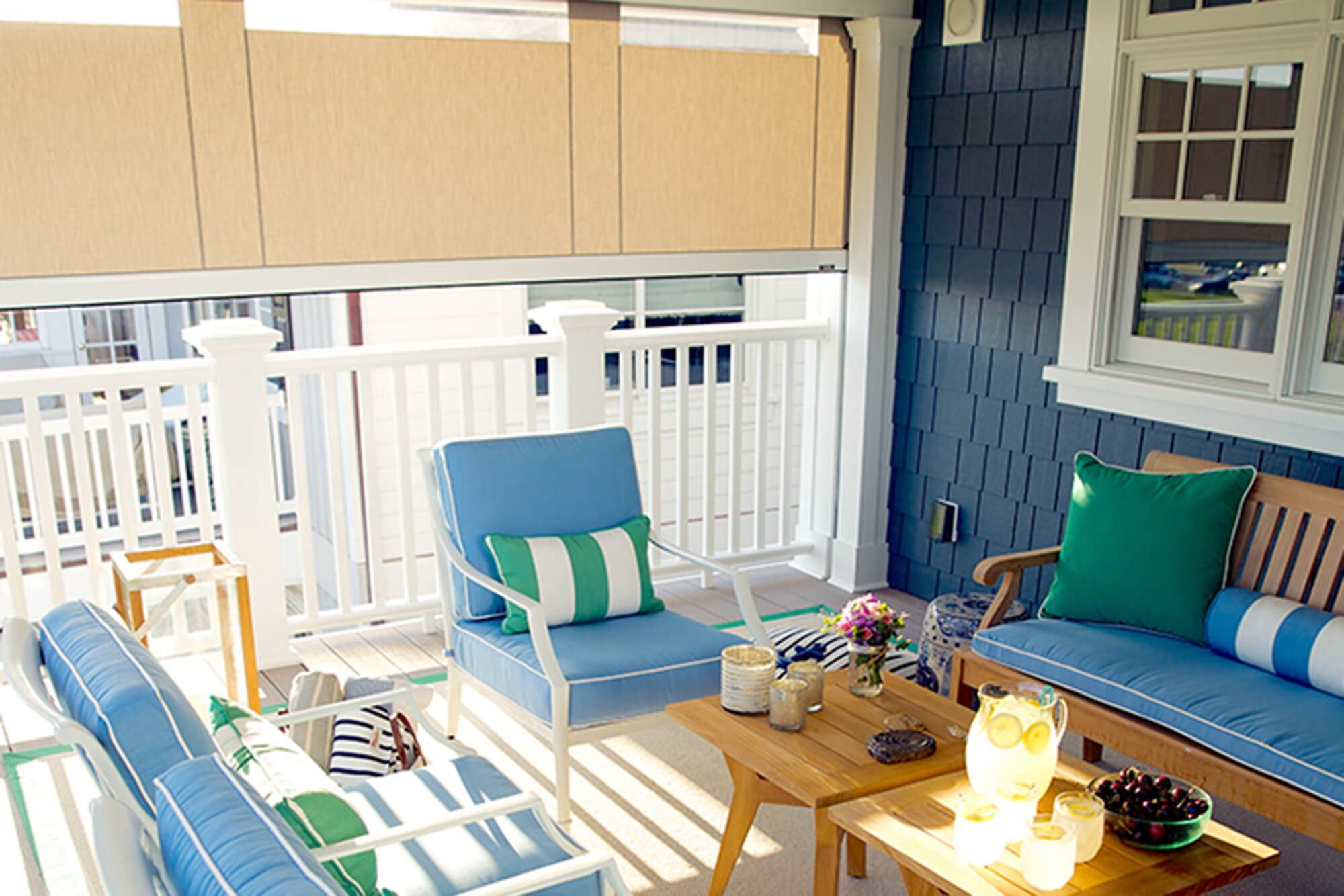 Tende da sole che si arrotolano realizzate con tessuti Sunbrella beige fanno ombra su terrazza con sedili in tessuto per tappezzeria Sunbrella blu