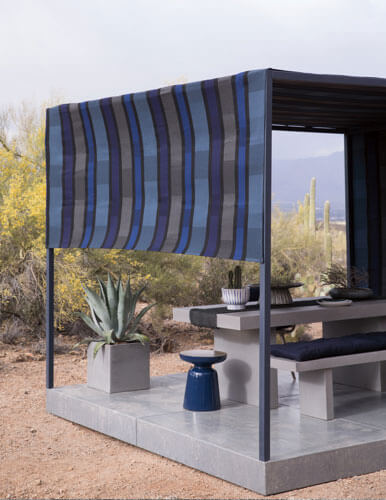 Utomhusbild i Arizona-öknen som visar en modern pergola med Sunbrella solskyddstyg skyddande över ett middagsbord och bänkar.