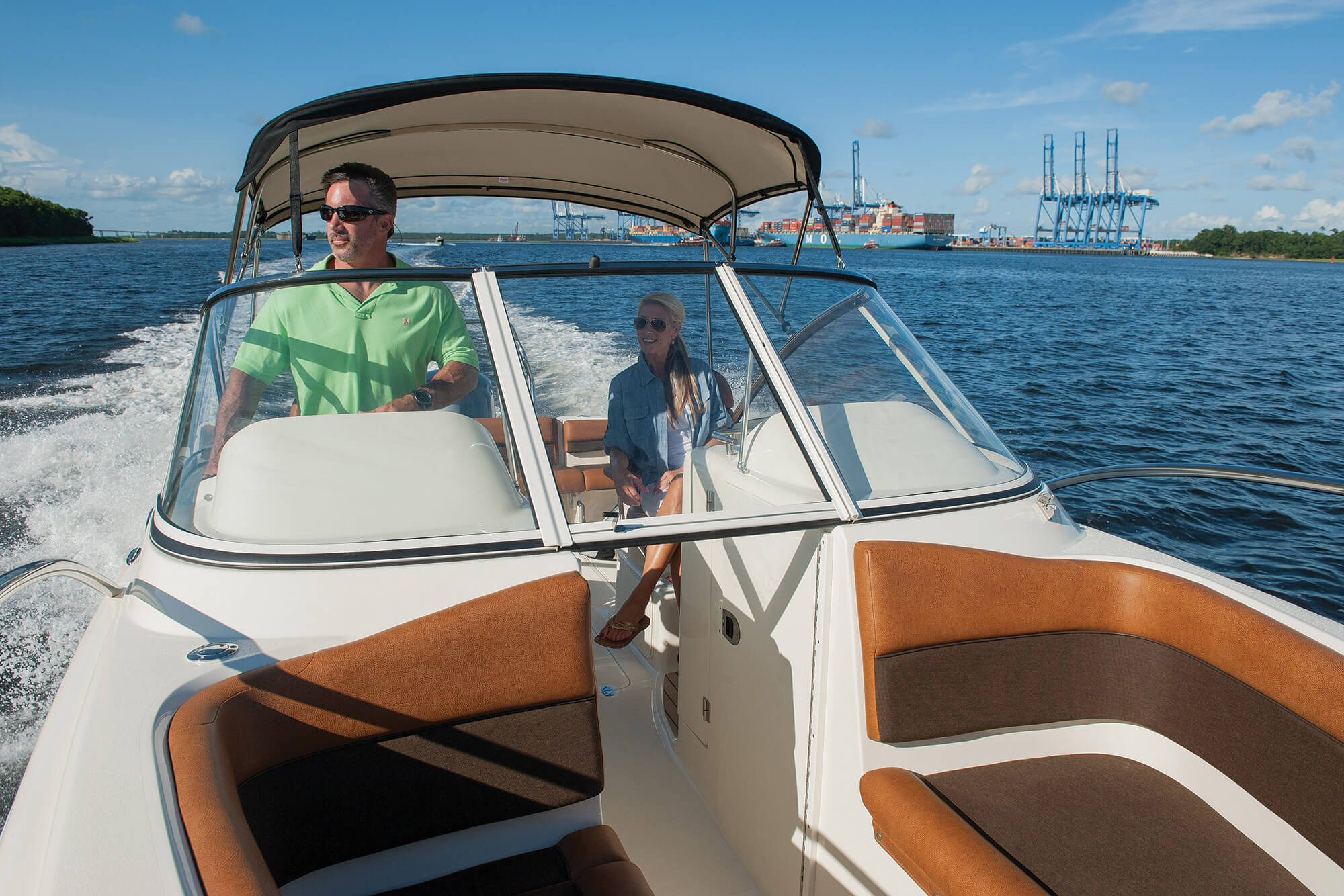 Couple sur un bateau à moteur avec un bimini en tissu Sunbrella Supreme et coussins marrons sur la proue