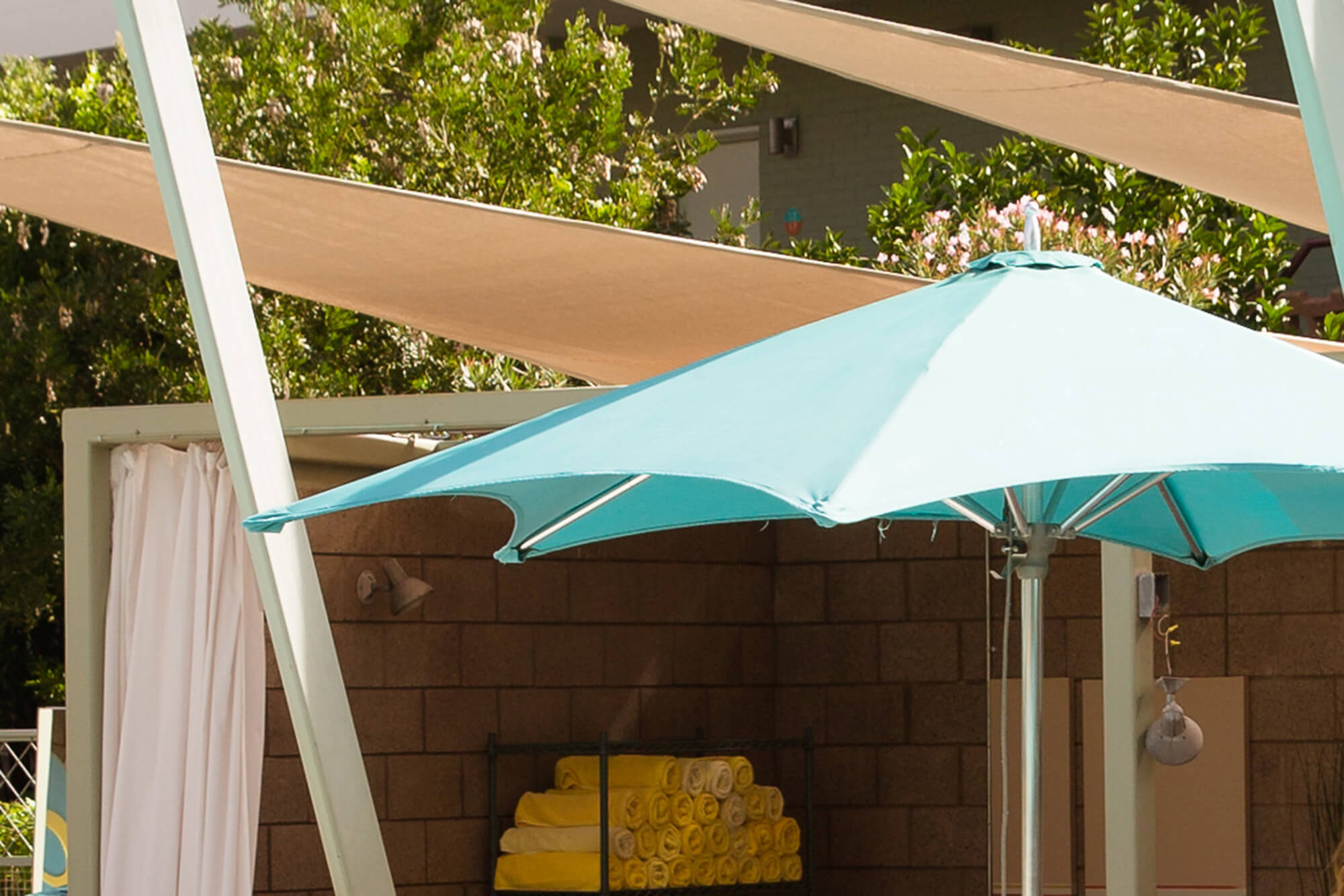 Parasol met blauw-groene Sunbrella-stof naast een hotelzwembad