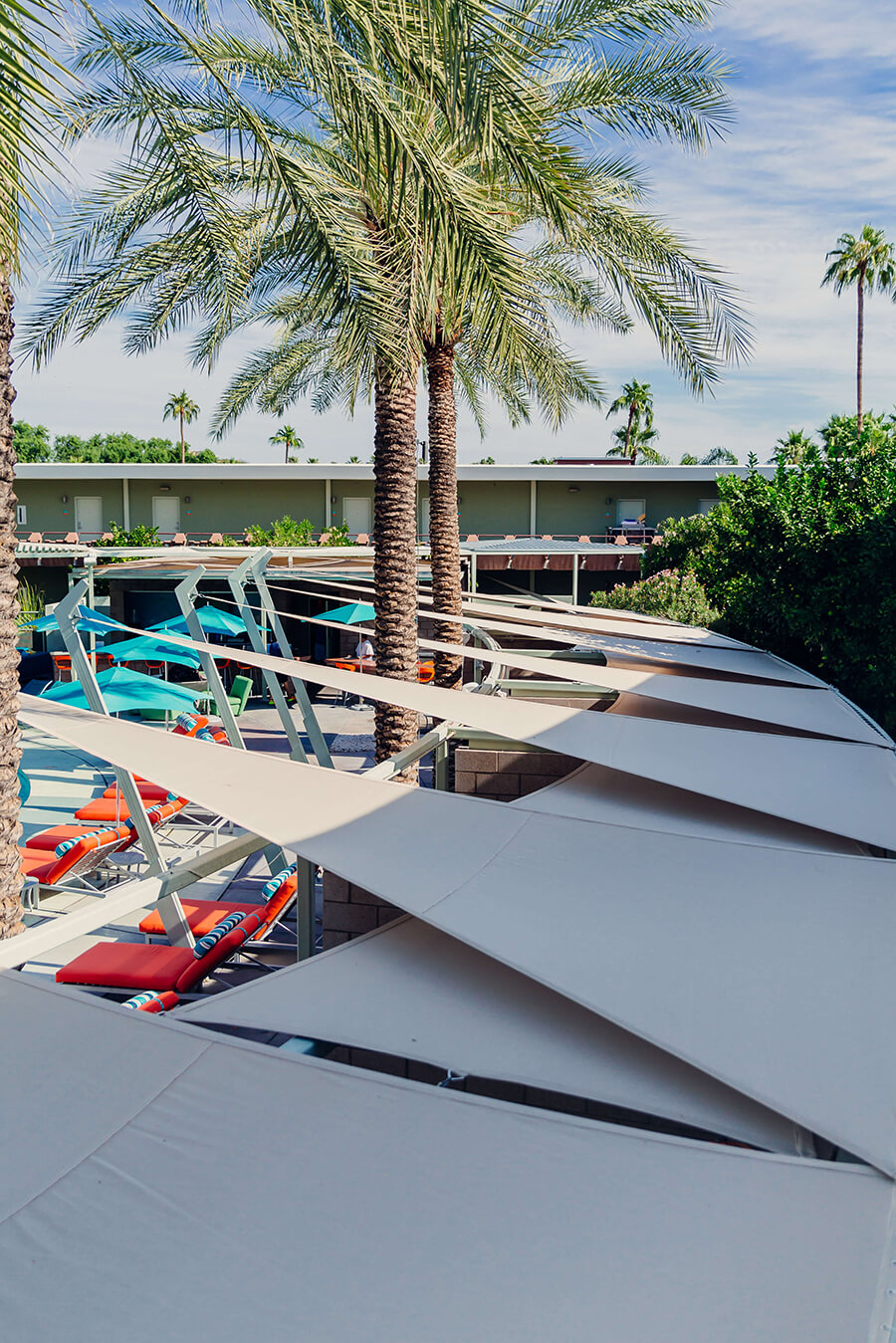 Schaduwdoeken met beige Sunbrella Contour-stof, geïnstalleerd bij een hotelzwembad met palmbomen op de achtergrond.