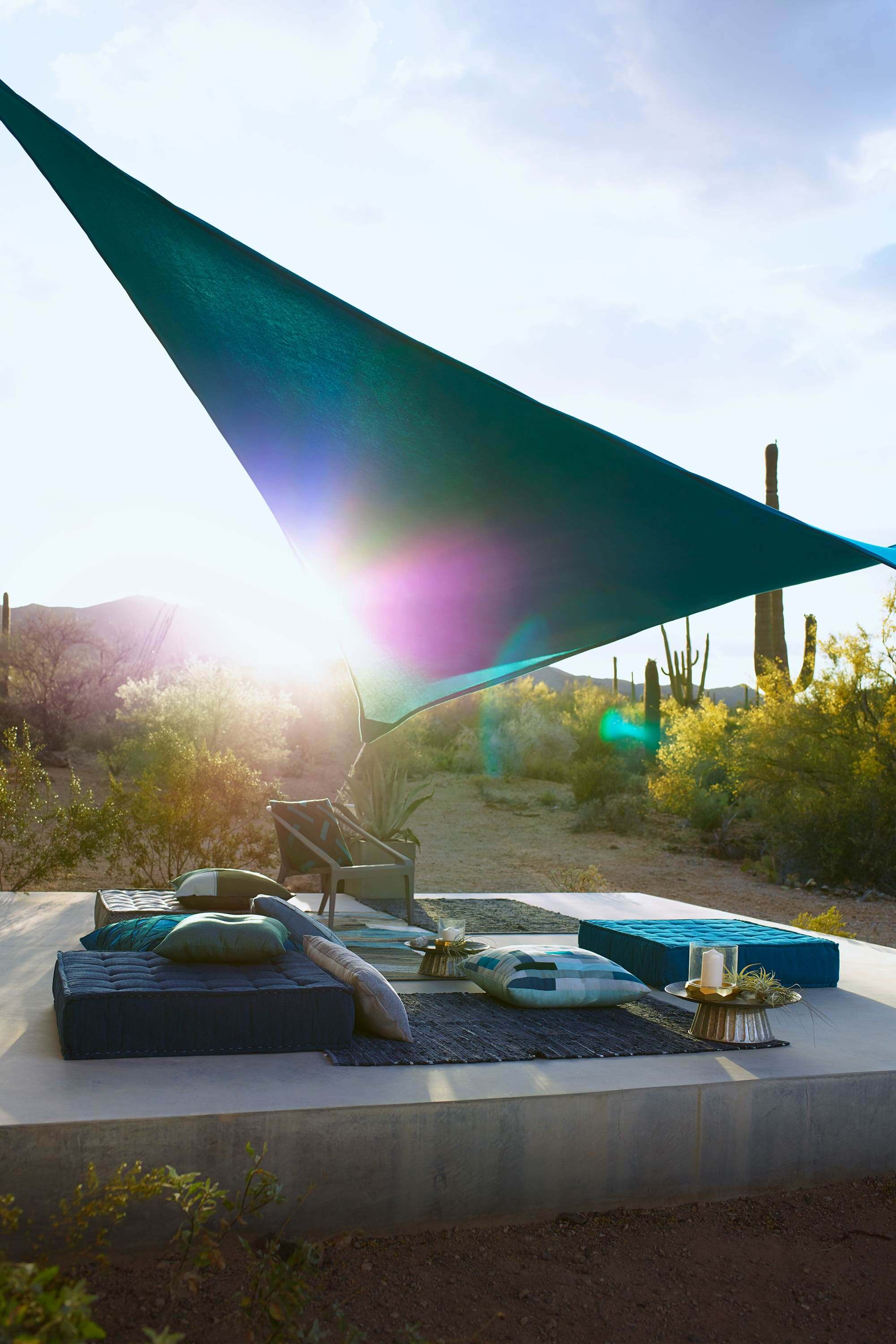 Outdoor seating of floor pillows covered with shade sail made using teal Sunbrella Contour fabric