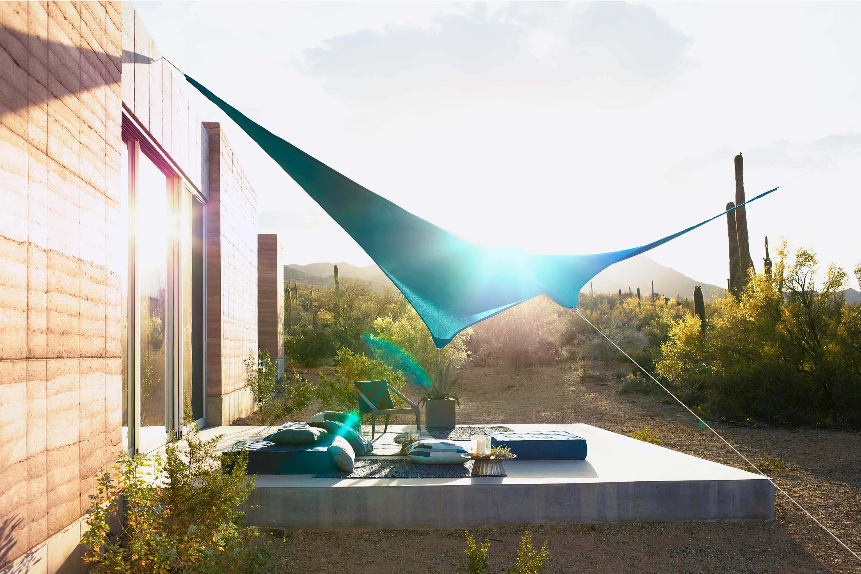 Un patio all’aperto nel deserto coperto da una vela parasole realizzata usando il tessuto Sunbrella Contour verde acquamarina