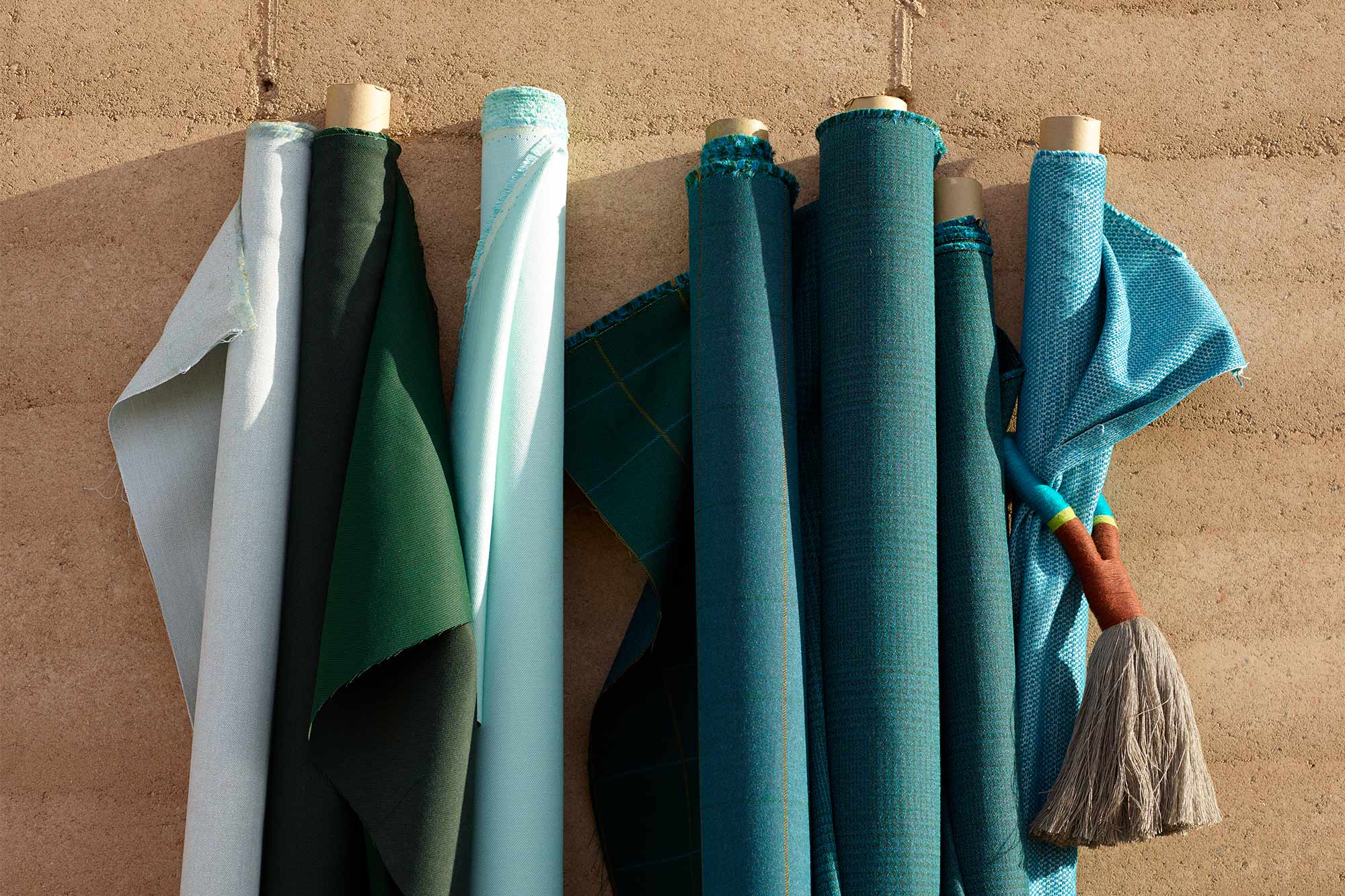 Rollos de telas Sunbrella para tapicería de color verde azulado contra una pared en el exterior