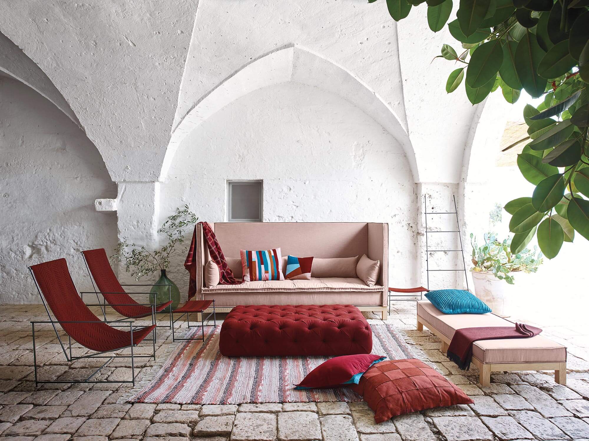 Uma sala de estar com um grande sofá, cadeiras e um otomano adornado em tons de vermelho e rosa são feitas usando tecido de estofamento Sunbrella.