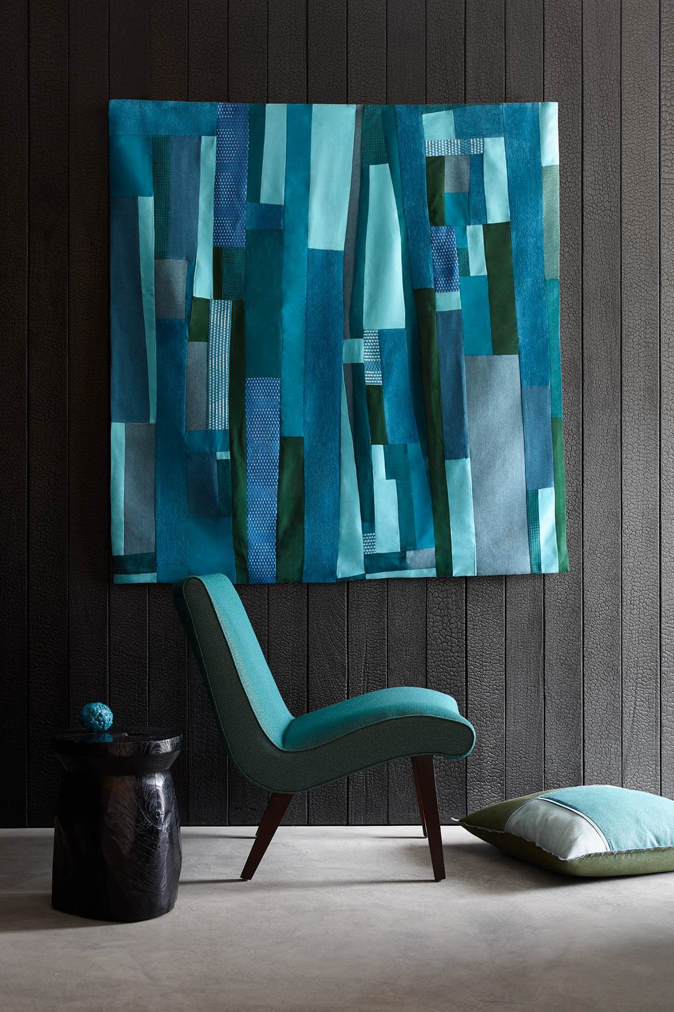 Poltrona estofada em tecido azul-petróleo, com peça decorativa na parede em tecido para estofamento Sunbrella, na cores azul e verde