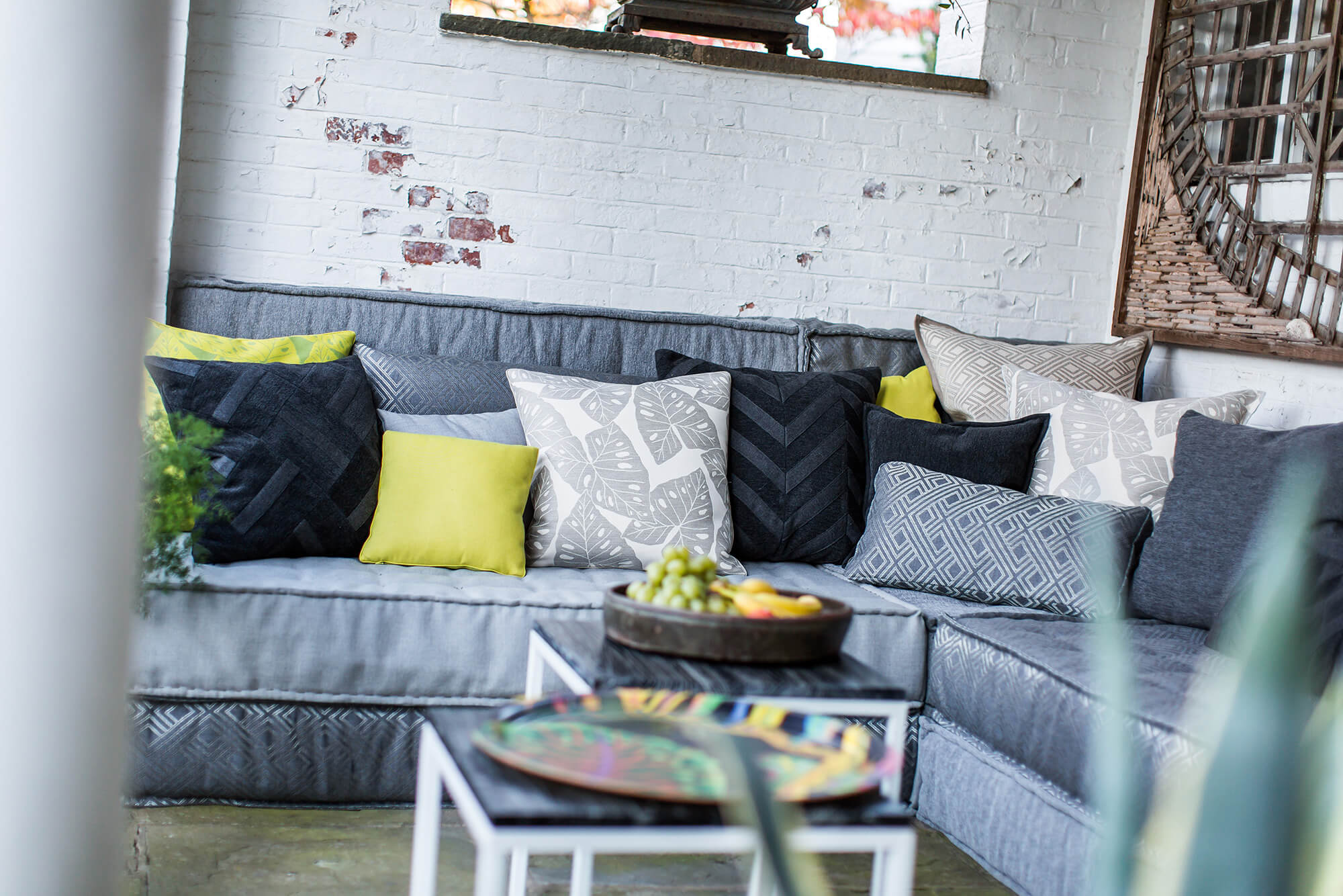 Outdoor-Sofa mit grauen Polstern und vielen grauen Kissen sowie einige grüne Akzentkissen
